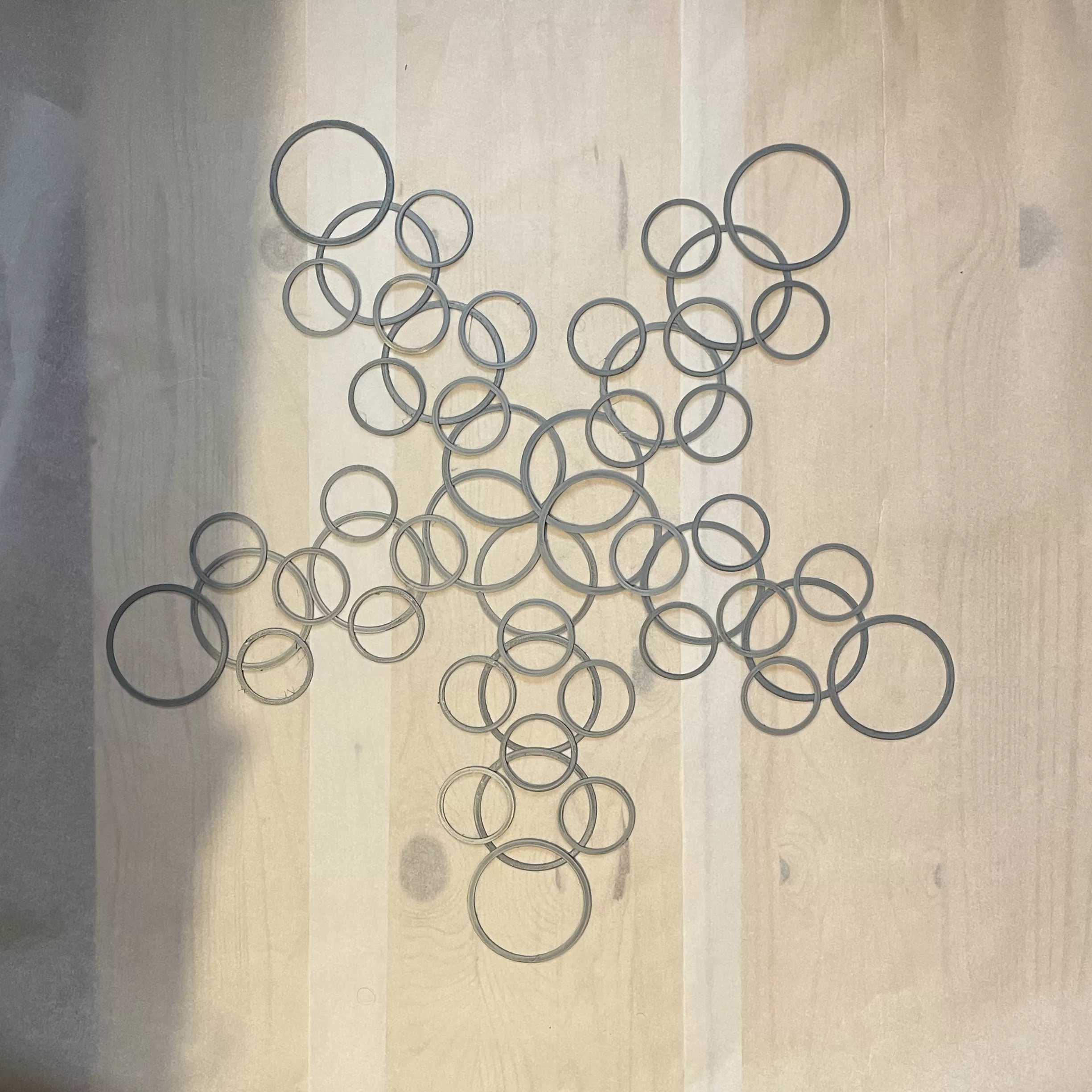 Silver PLA rings laid out by hand in a star pattern on a wooden table