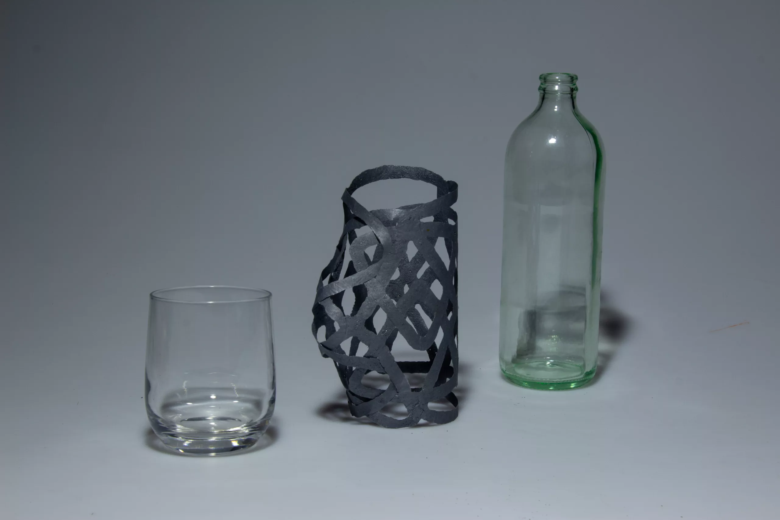 A dark PLArt sleeve between a glass and a bottle