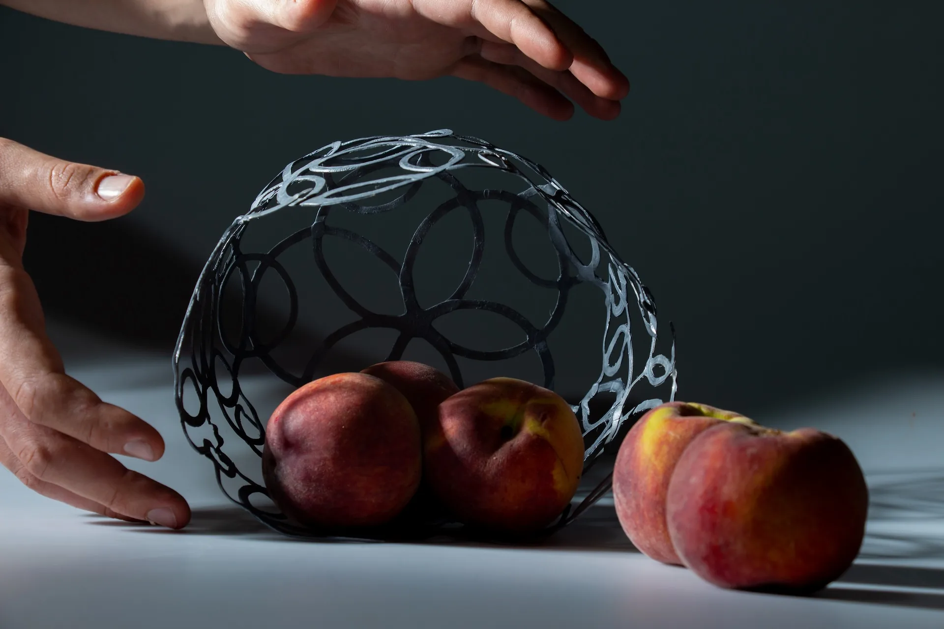 Two hands around the fruit bowl, lit from the side